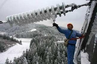 A power employee hammers at the ice covering a pylon, insulators and conductors