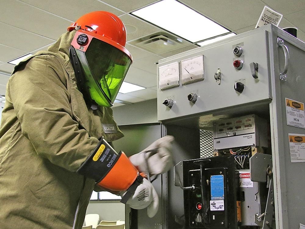 Racking medium voltage circuit breaker by maintenance engineer wearing fire-resistant arc-rated PPE