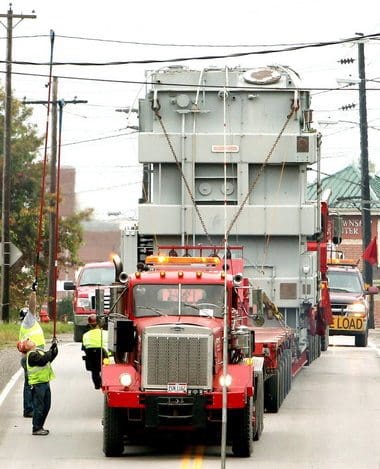 Workers move wires, lights, and poles to transport a 340-ton power transformer, causing hours of traffic delay